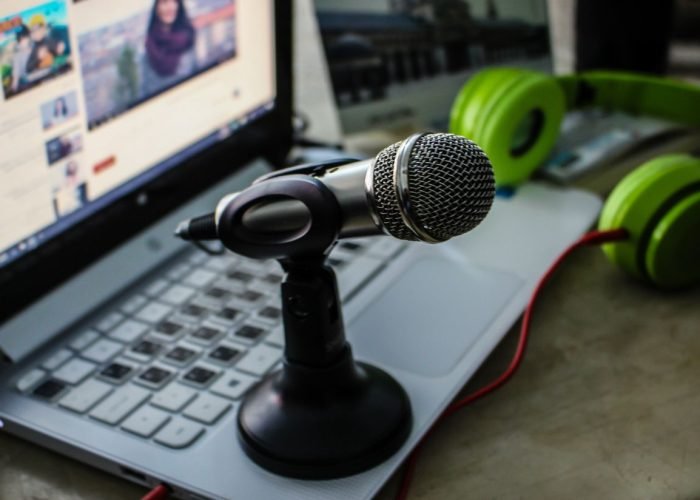 Close-up of a podcasting setup with a microphone, laptop, and green headphones.