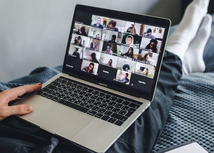 Adult sitting on bed using laptop for video conference and note-taking.